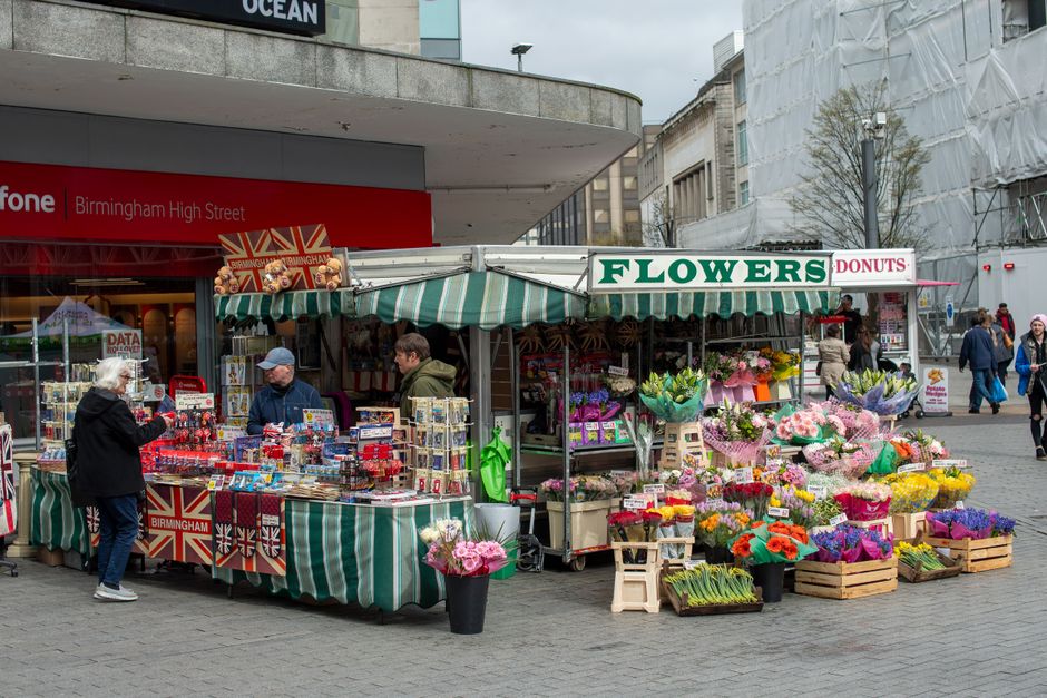 A street-side floral stall at West Brompton markets featuring a variety of fresh flowers including pink roses, purple tulips, orange gerbera daisies, and other colourful blooms arranged in wooden crat